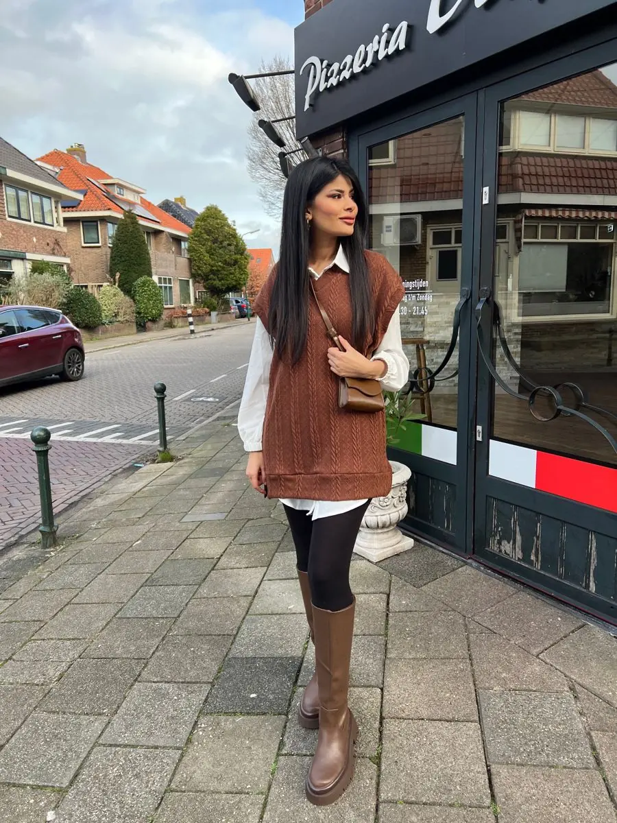 Mulher com colete marrom, legging preta e bota cano alto
