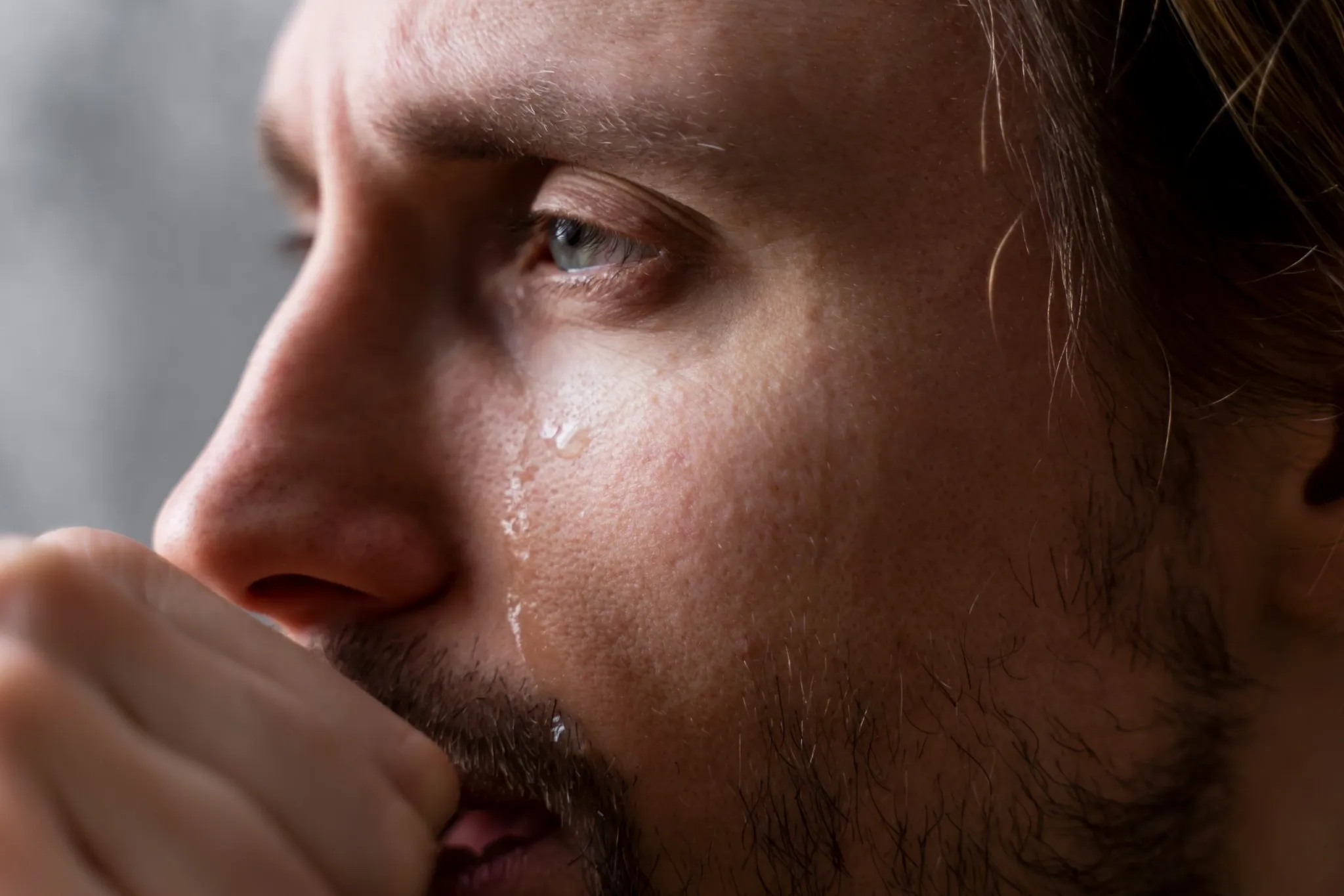 Homem com expressão de tristeza, com uma lágrima escorrendo pela face enquanto parece estar lidando com um momento emocional intenso.