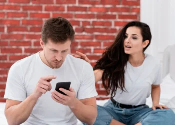 Mulher tentando chamar a atenção do namorado que está distraído com o celular, refletindo sobre as expectativas em relacionamentos reais versus os casais perfeitos das redes sociais.