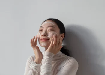 Mulher sorrindo enquanto aplica creme facial, com foco em sua rotina de skincare coreano para uma pele saudável.