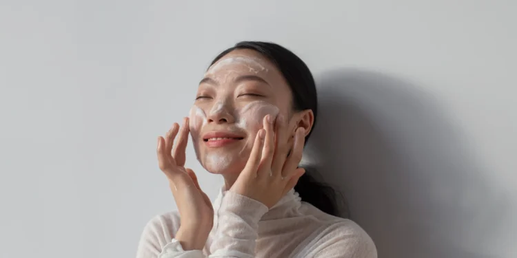 Mulher sorrindo enquanto aplica creme facial, com foco em sua rotina de skincare coreano para uma pele saudável.