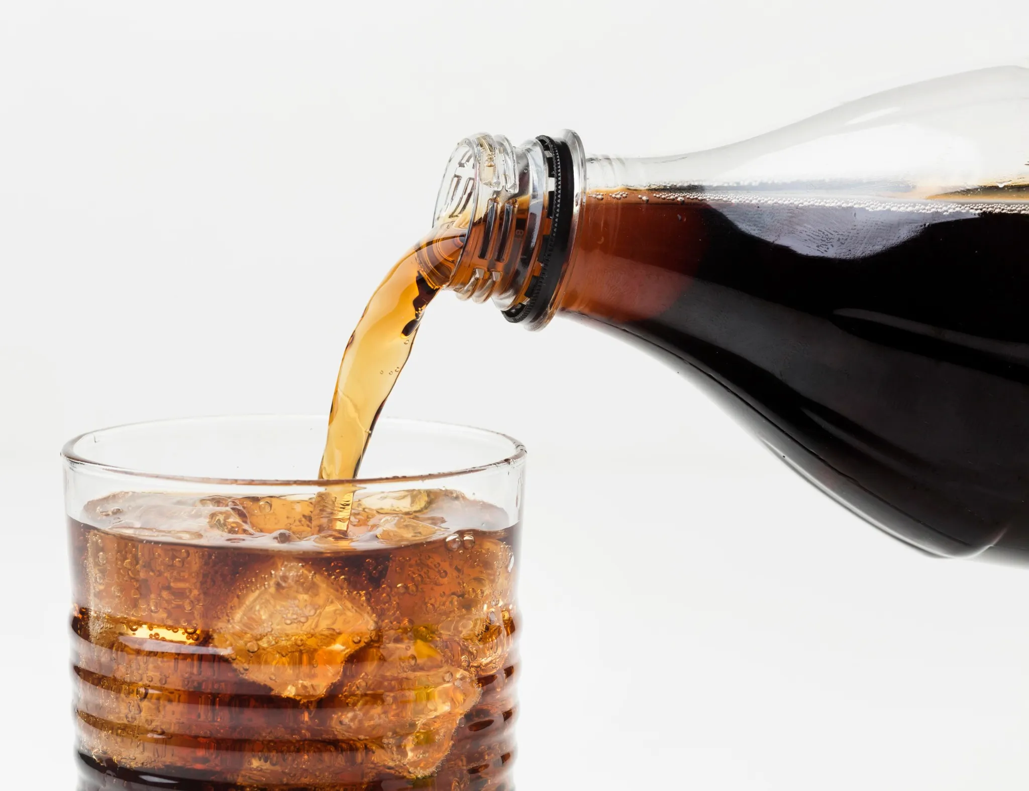 Imagem de refrigerante sendo servido em um copo, com gelo, representando os riscos do consumo de bebidas adoçadas com aspartame.