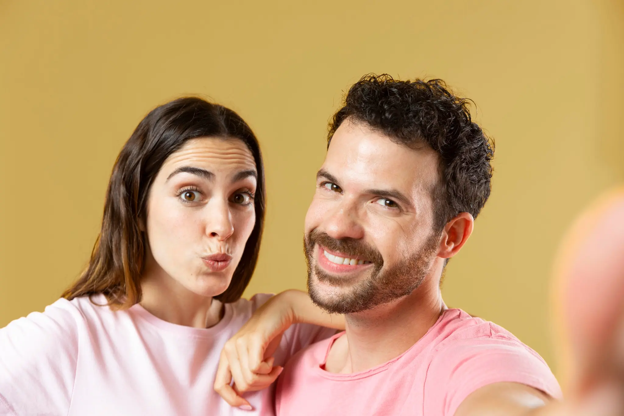 Casal sorrindo juntos, capturando um momento espontâneo e feliz em um fundo neutro.