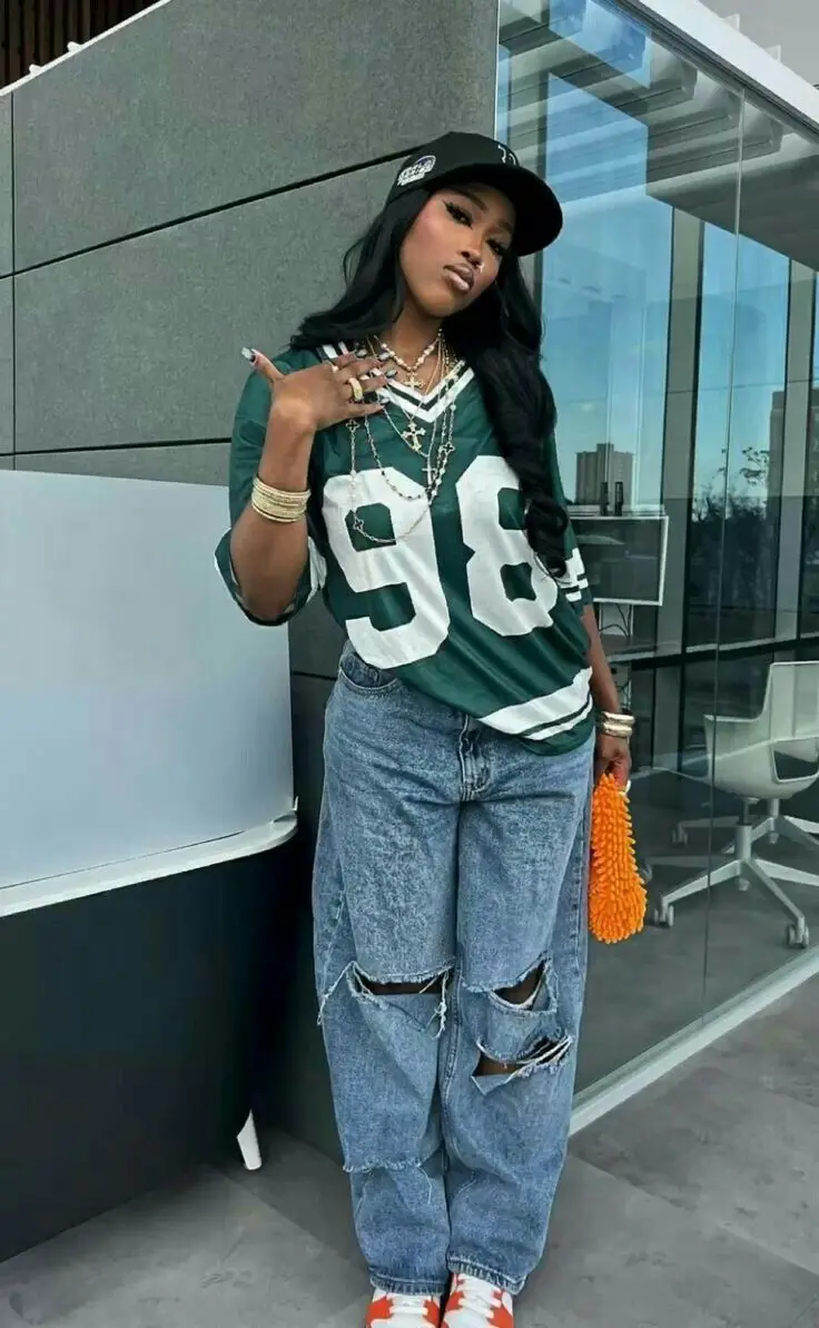 Mulher em look streetwear com camisa de time, calça e boné