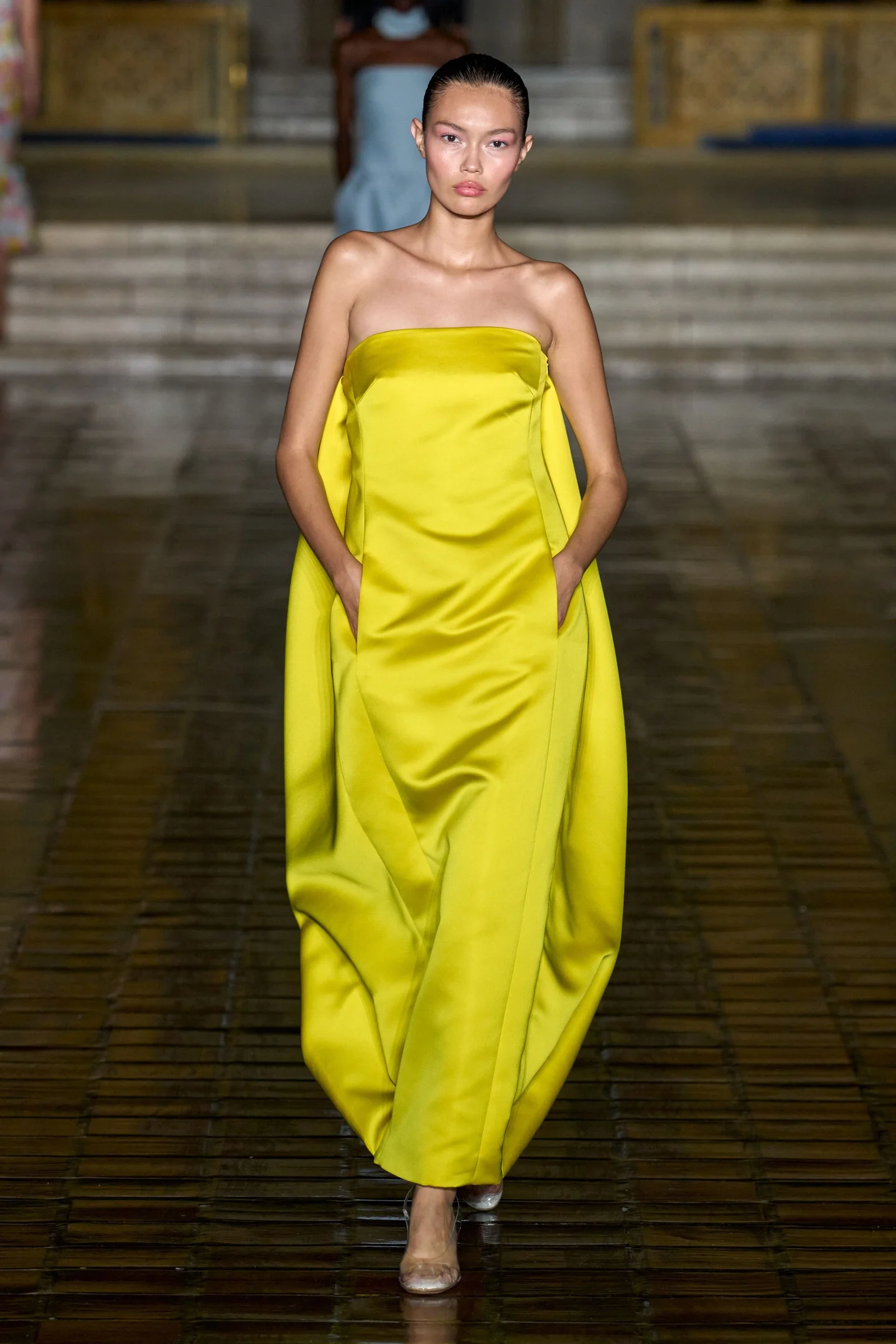 Modelo desfilando com vestido amarelo com efeito bubble, criando volumes arredondados, típico da tendência inflada da temporada.