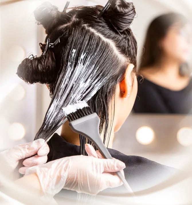 Profissional aplicando produto de alisamento em mechas de cabelo com um pincel em um salão de beleza.