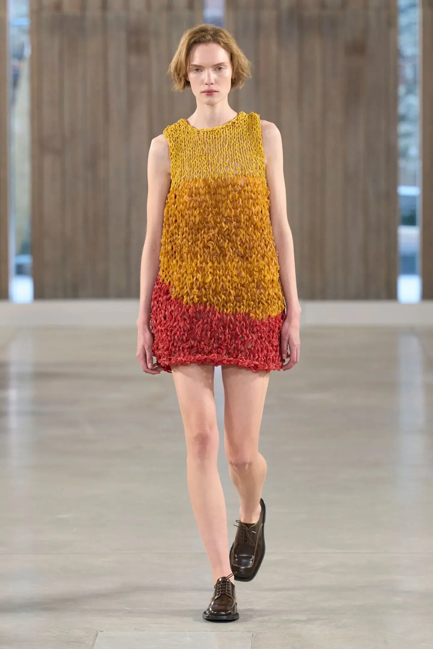Modelo desfilando com vestido artesanal de técnicas manuais em tons quentes, valorizando o trabalho artesanal na moda SS26.