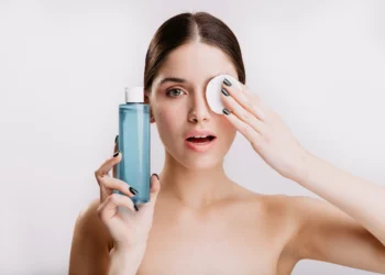 Mulher usando água micelar para limpar o rosto com um disco de algodão, aplicando o produto na rotina de skincare