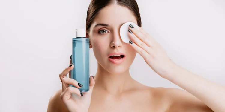 Água micelar: para que serve e como usar na sua rotina de skincare 1 Mulher usando água micelar para limpar o rosto com um disco de algodão, aplicando o produto na rotina de skincare