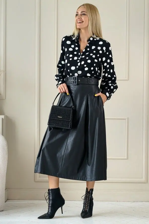 Mulher usando blusa de poá preta e branca com saia de couro midi preta