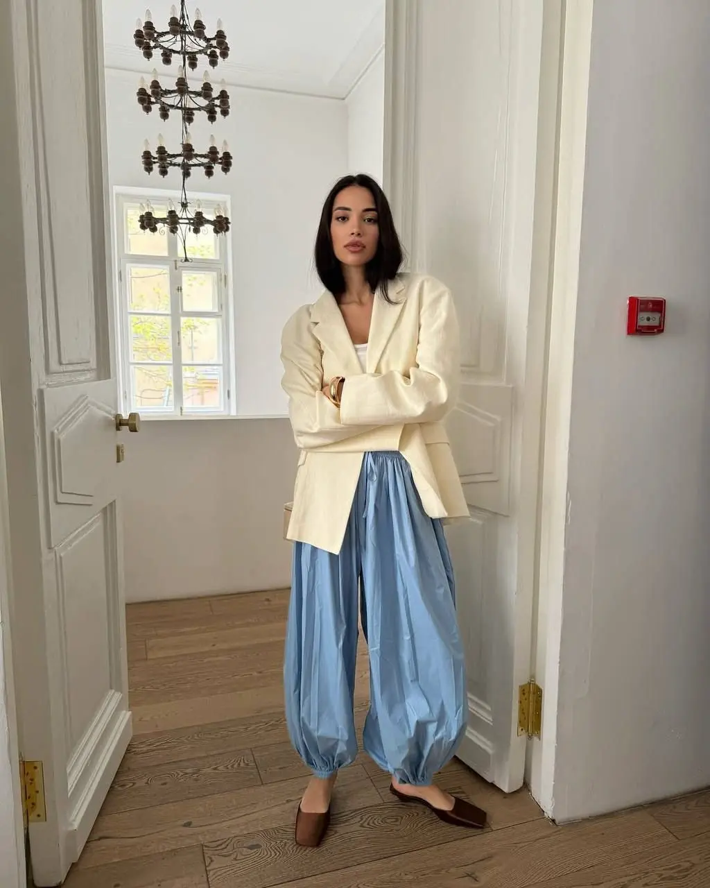 Mulher usando calça aladim azul com blazer branco em ambiente minimalista