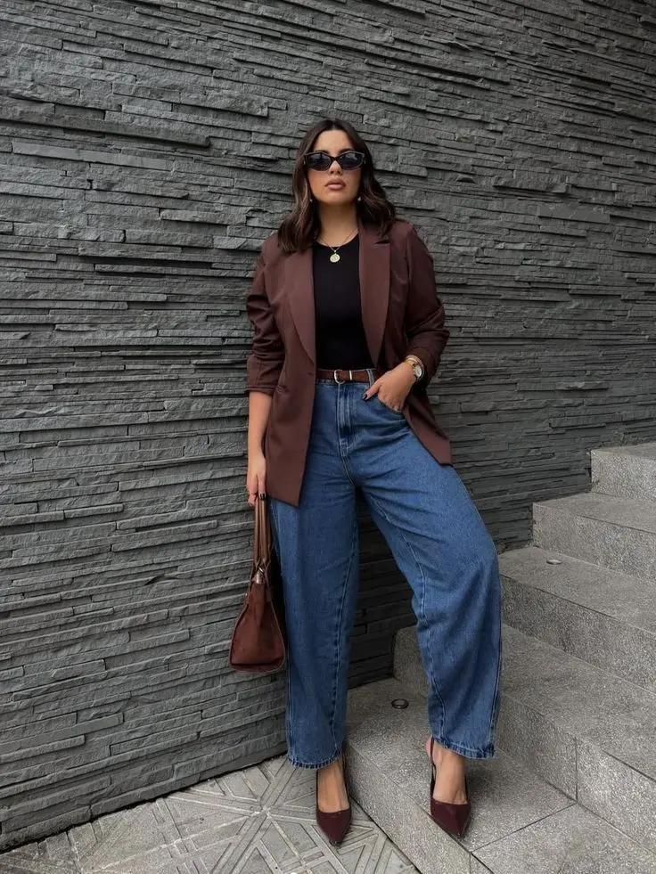 Look feminino com calça jeans escura e blazer de alfaiataria para evento formal ou social, acompanhado de scarpin e acessórios delicados.