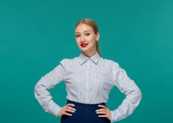 Mulher com camisa listrada, pose confiante com fundo verde, mostrando estilo de primavera e verão.
