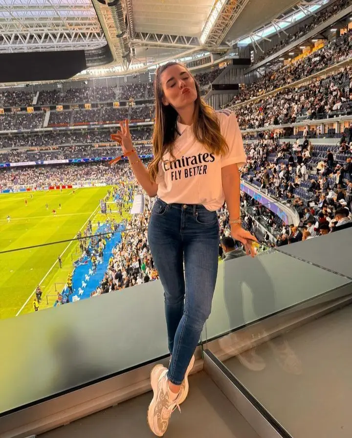 Mulher estilosa usando camisa de time com calça jeans e tênis branco em estádio lotado