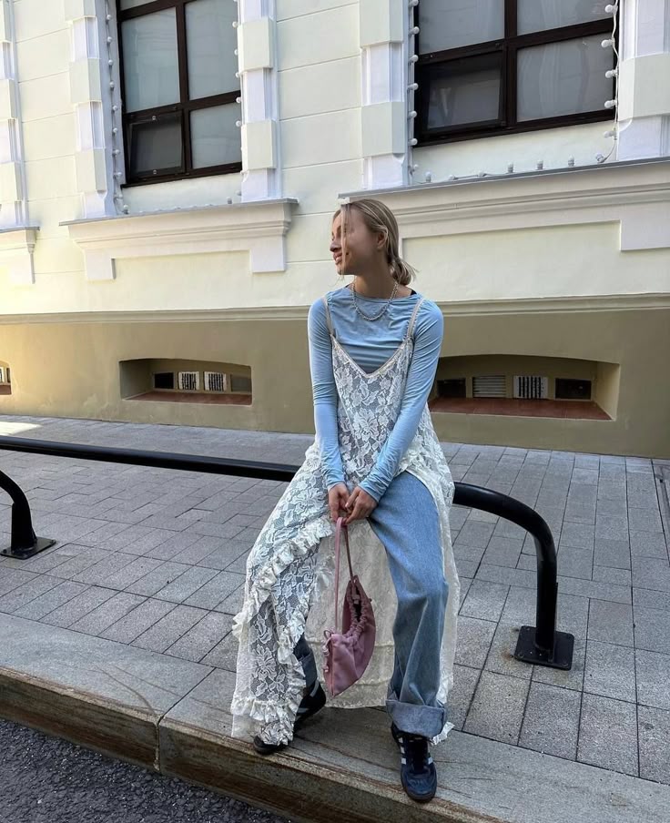 Mulher usando um vestido de renda sobre uma blusa de manga comprida azul-claro e calça jeans.