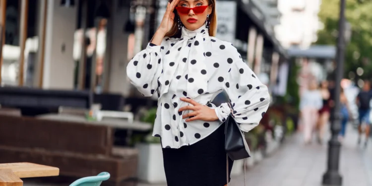 Mulher estilosa com blusa de poá e saia preta em look elegante na rua
