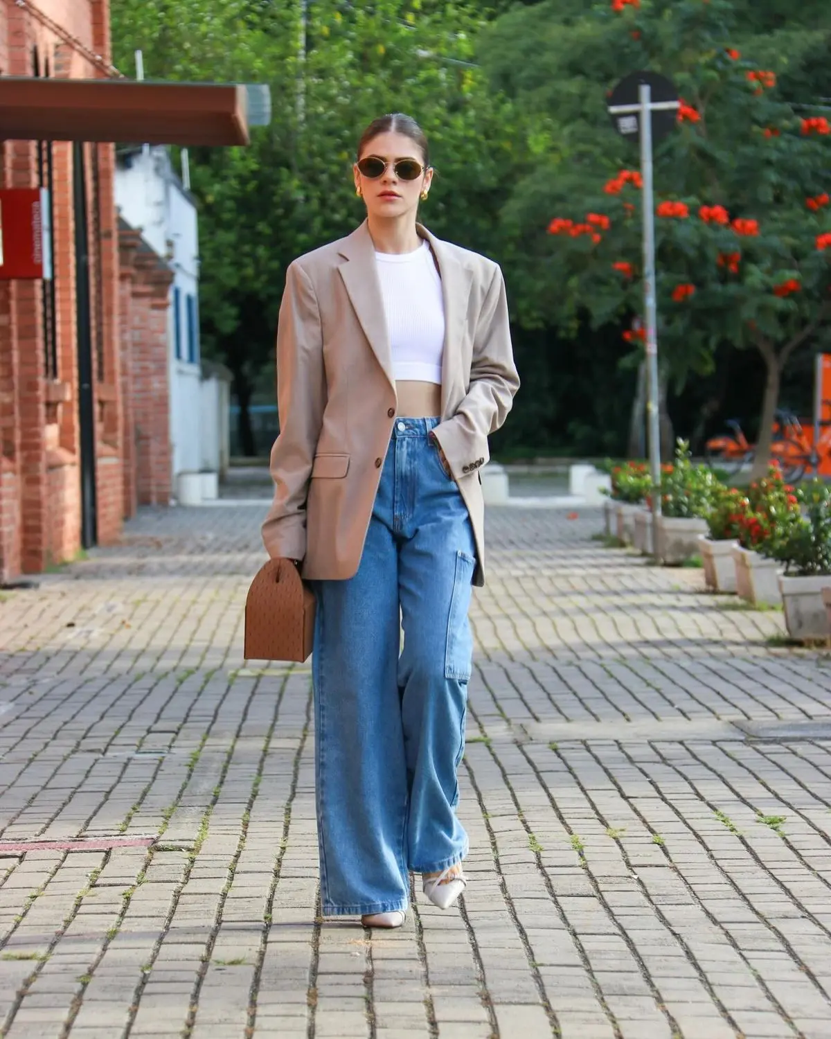 Mulher jovem em blazer oversized, regata branca e jeans, posando em uma rua da cidade.