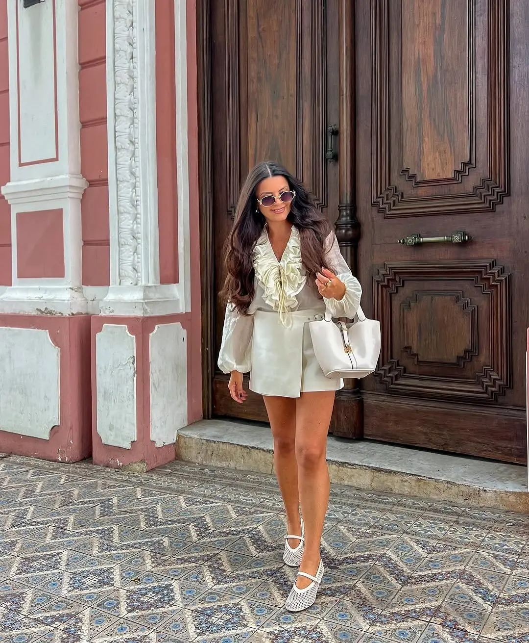 Mulher com um look elegante, usando blusa de seda branca e sapatilhas de balé, caminhando.