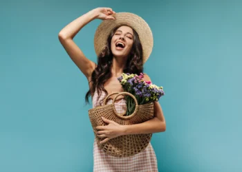 Mulher sorrindo com flores na cesta, vestindo chapéu, simbolizando a chegada da primavera.
