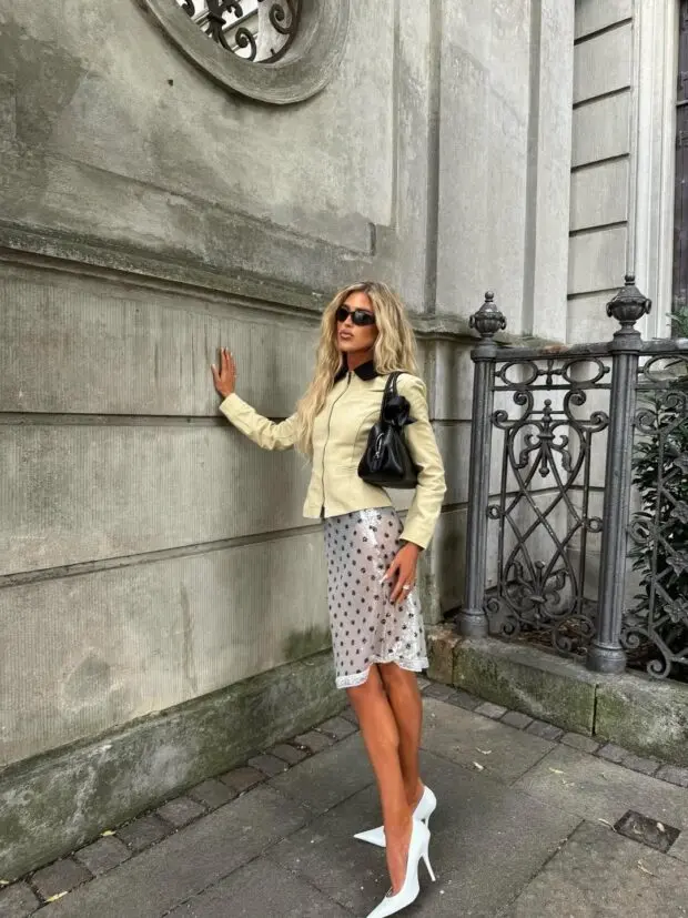 Mulher com look elegante usando saia de polka dots transparente, jaqueta clara e scarpin branco.
