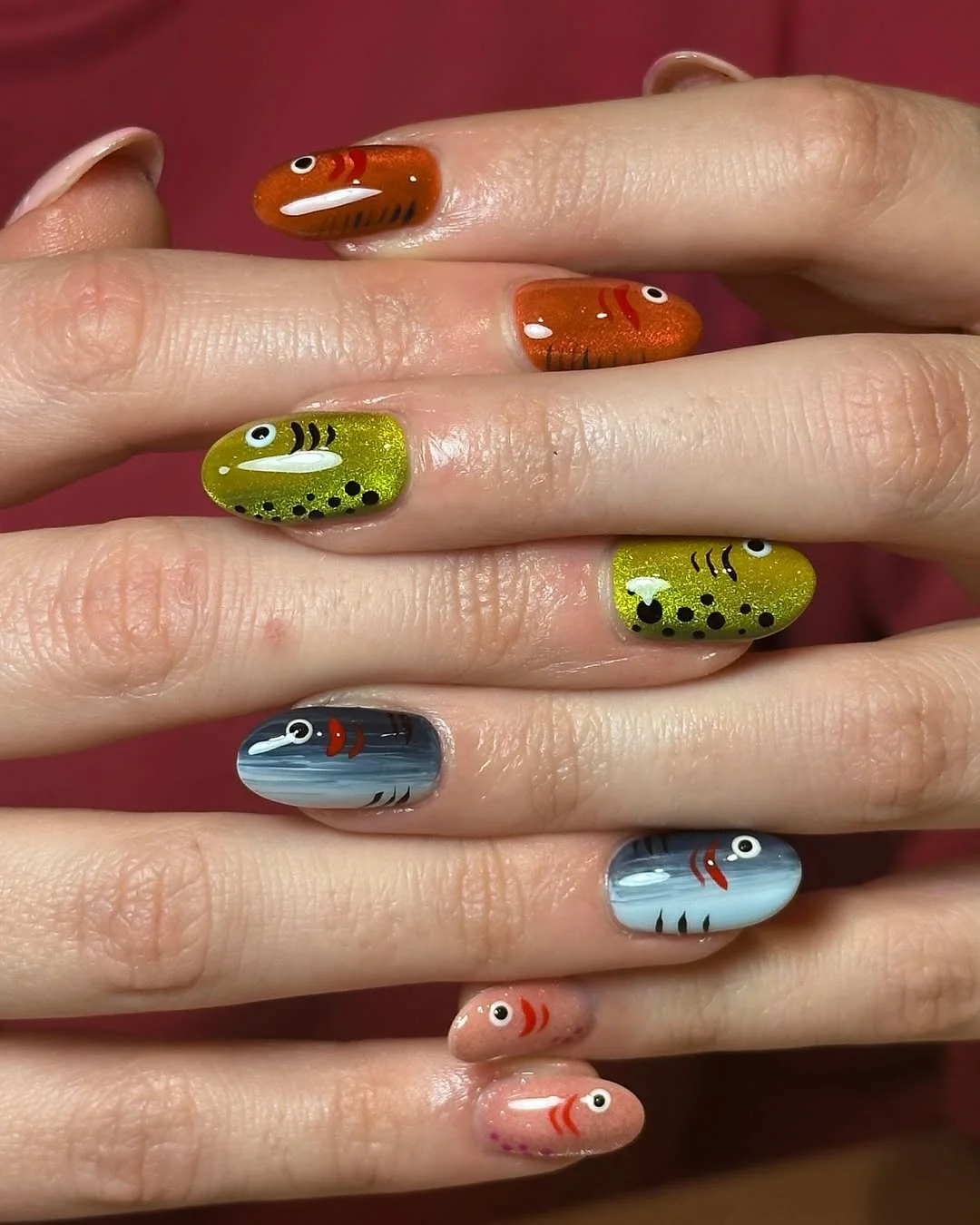 Unhas decoradas com desenhos de peixes em esmalte cat eye, com efeitos brilhosos e cores vibrantes.