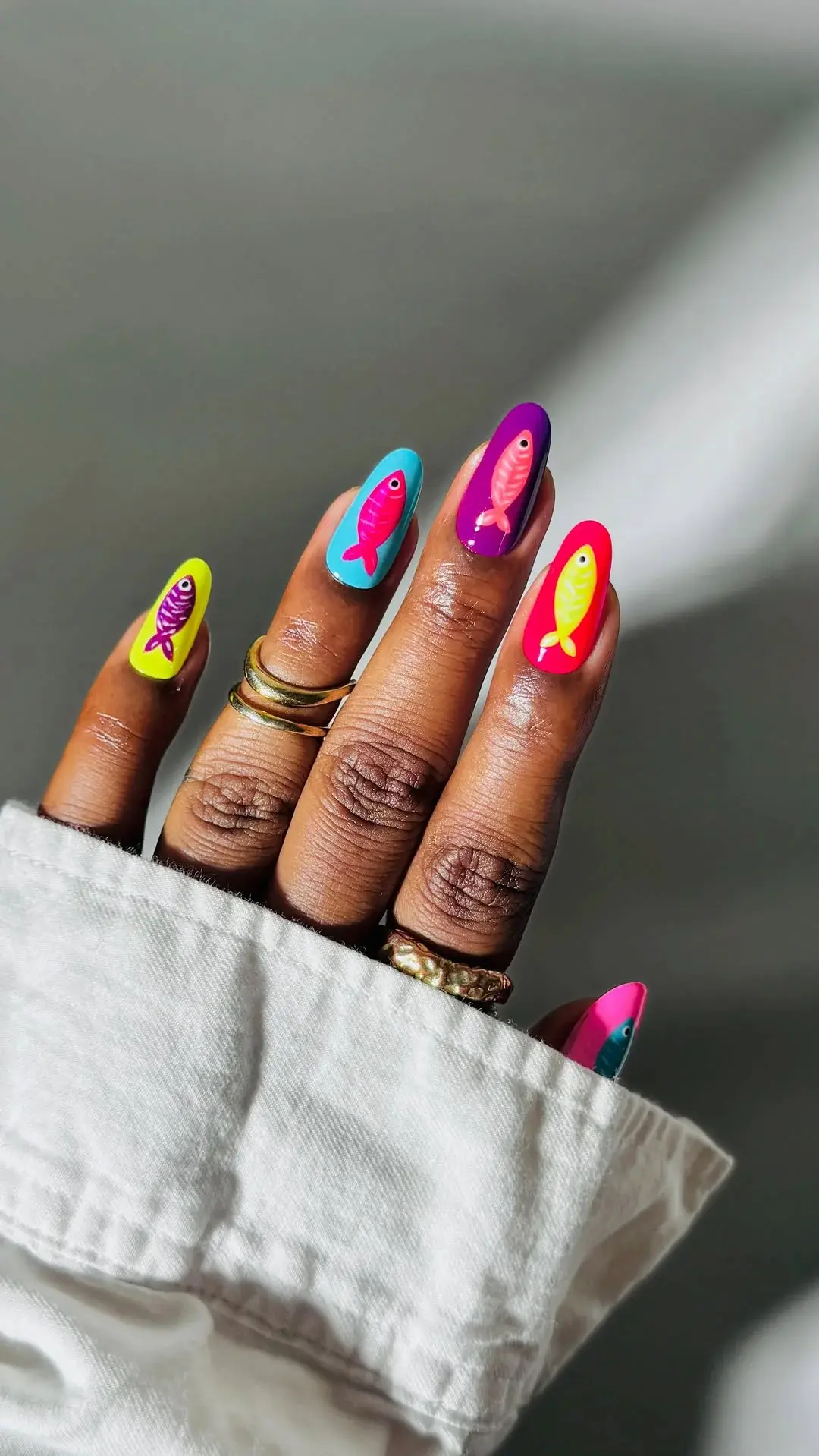 Imagem de unhas com design colorido de peixes, em tons vibrantes como roxo, azul, amarelo e rosa.