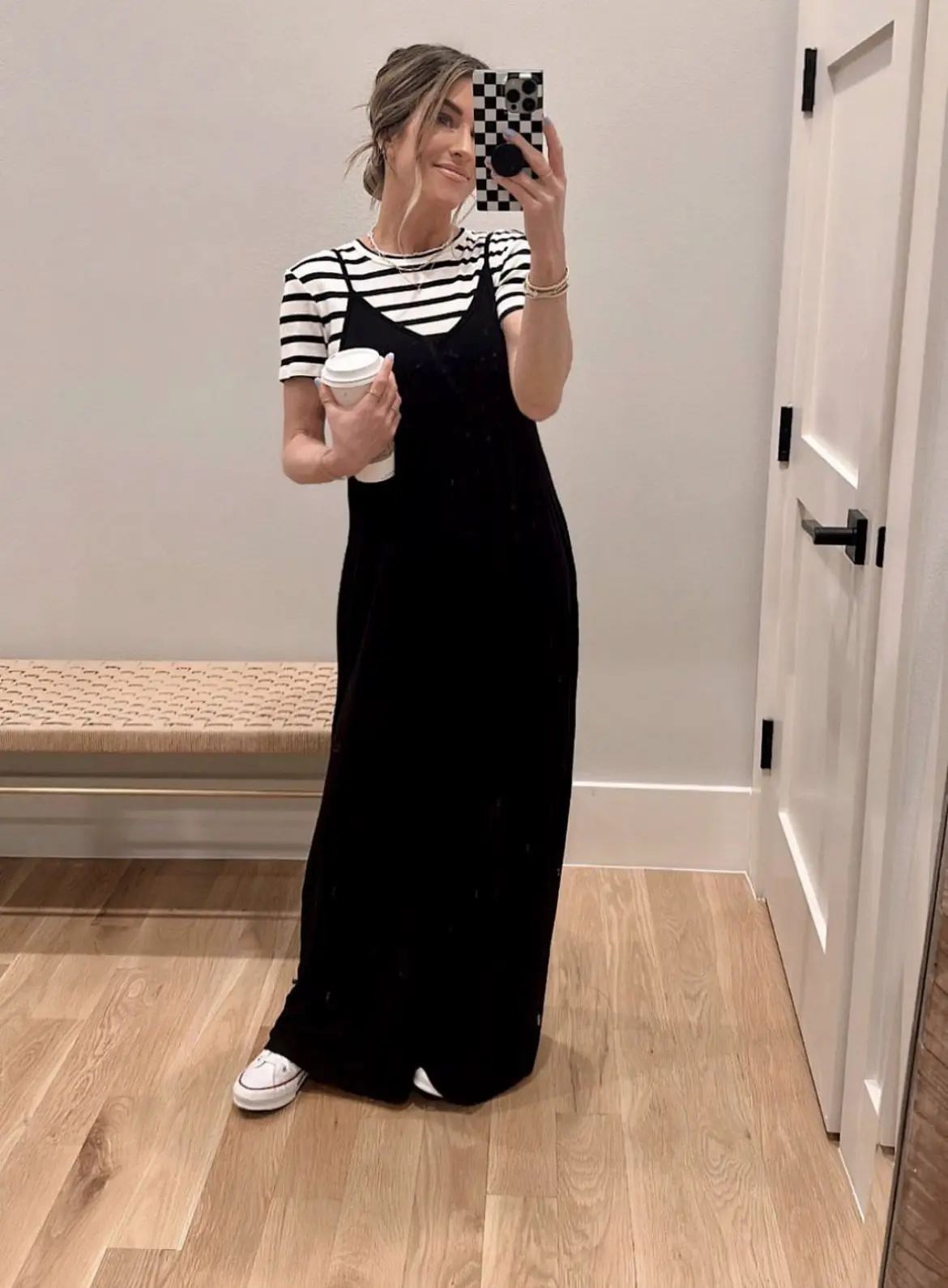 Mulher usando vestido preto por cima de camisa listrada, criando um look romântico e moderno, com tênis branco.