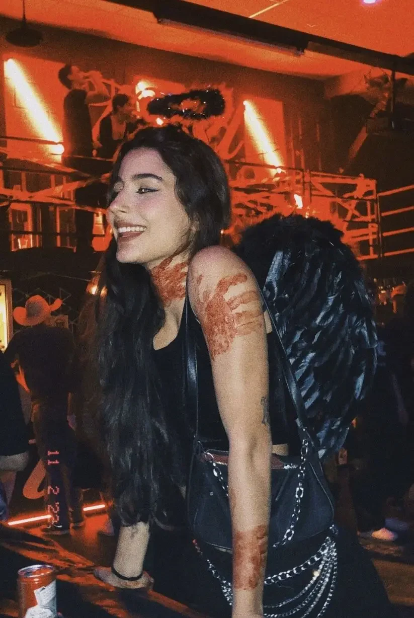 Mulher usando fantasia de anjo sombrio com asas pretas e maquiagem dramática em uma festa.