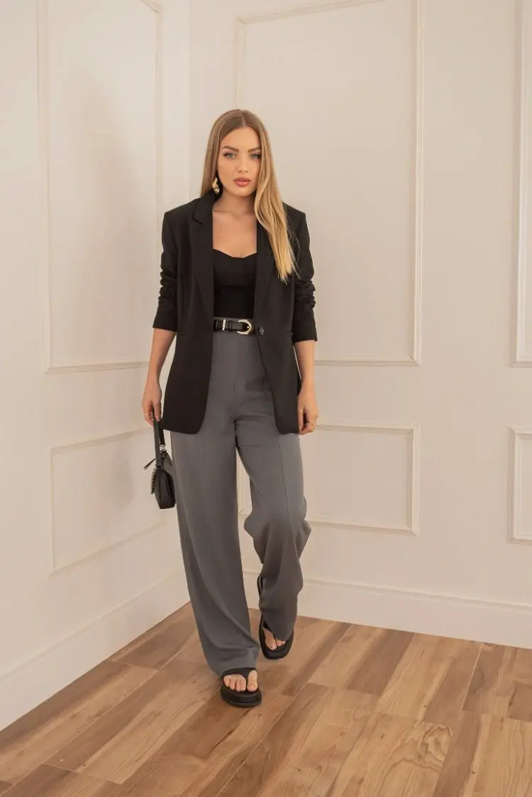 Mulher usando calça de alfaiataria cinza com blazer preto e blusa preta.