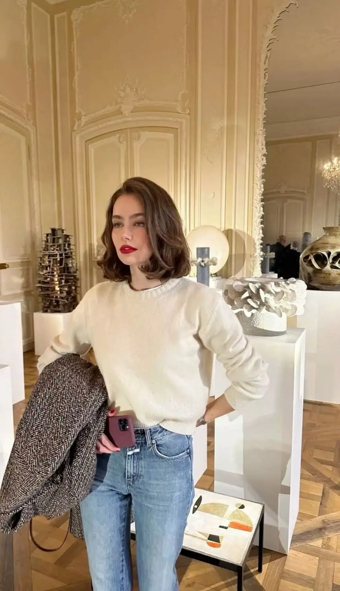 Mulher com cabelo estilo Collarbone Lob em ambiente de arte moderna, usando suéter branco e jeans.