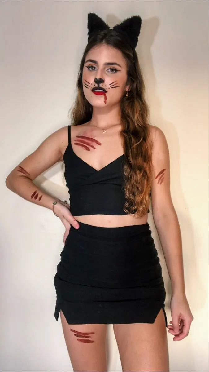 Fantasia de gatinha clássica para Halloween com maquiagem de arranhões e roupa preta.
