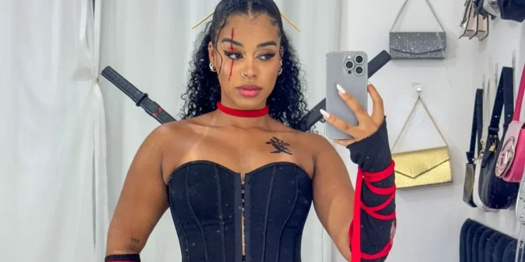 Mulher com fantasia de ninja, com vestido preto, fita vermelha e acessórios, posando para foto.