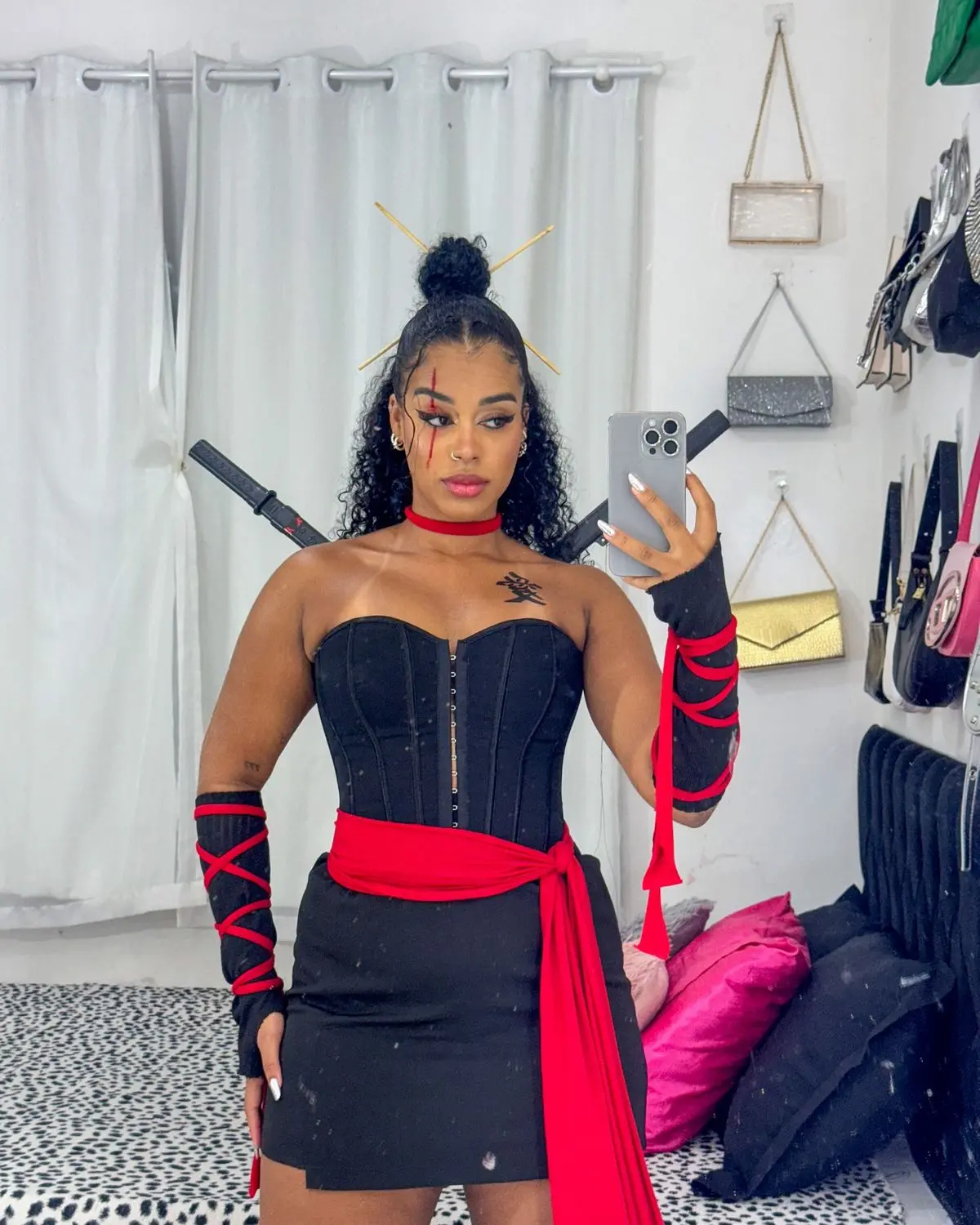 Mulher com fantasia de ninja, com vestido preto, fita vermelha e acessórios, posando para foto.