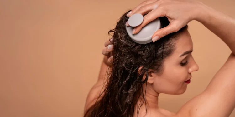 Mulher aplicando escova de massagem no couro cabeludo para cuidados capilares.