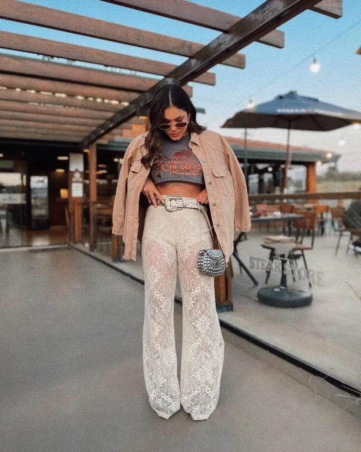 Mulher com calça de renda, cinto e bolsa estilizados, criando um look moderno com acessórios statement.