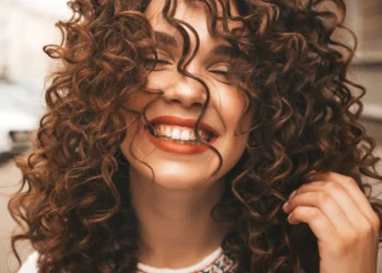 7 dicas simples para dar volume ao cabelo e deixar seus fios incríveis 11 Mulher sorrindo ao lado de fios de cabelo cacheados, representando dicas para aumentar o volume do cabelo.