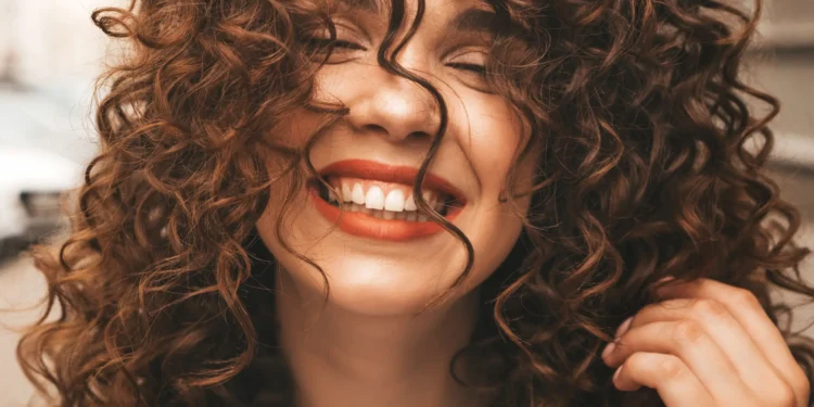 Mulher sorrindo ao lado de fios de cabelo cacheados, representando dicas para aumentar o volume do cabelo.