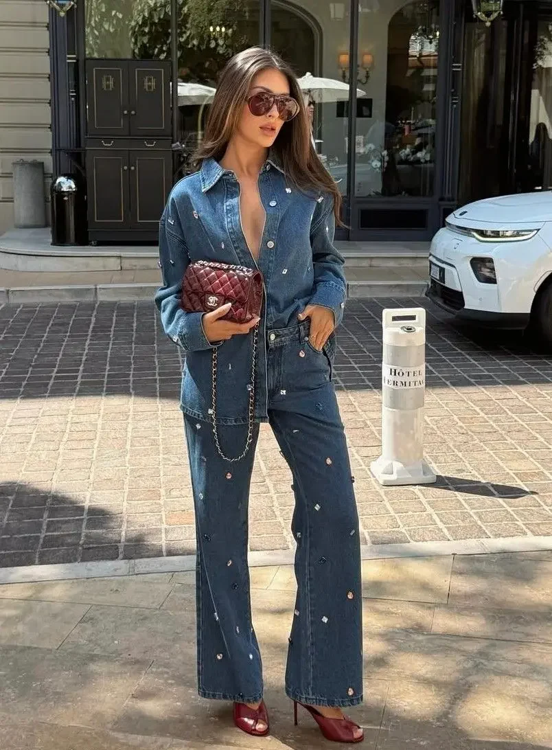 Conjunto jeans com aplicações bordadas, bolsa vinho e salto alto — look urbano sofisticado.