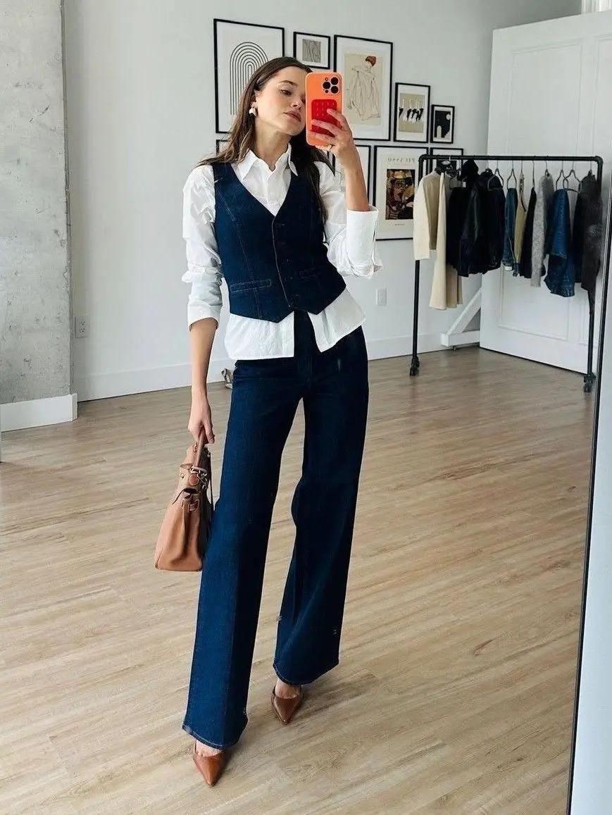 Look moderno com colete jeans sobre camisa branca, combinado com calça jeans e acessórios discretos, mostrando a versatilidade do estilo urbano.