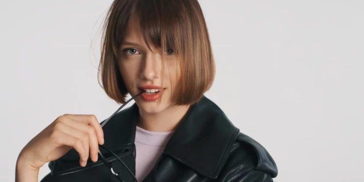 6 cortes de cabelo femininos tendência para 2026 — escolha o seu estilo 1 Mulher com corte de cabelo moderno e estilo ousado, vestindo jaqueta de couro e óculos, com sorriso confiante.