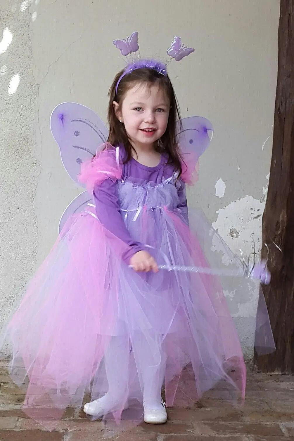 Criança com fantasia de fada encantada, usando vestido roxo e asas lilases.