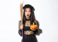 Sem gastar muito: fantasias de Halloween caseiras que você monta rapidinho 7 Mulher com expressão surpresa vestida de bruxa segurando abóbora e vassoura para Halloween.