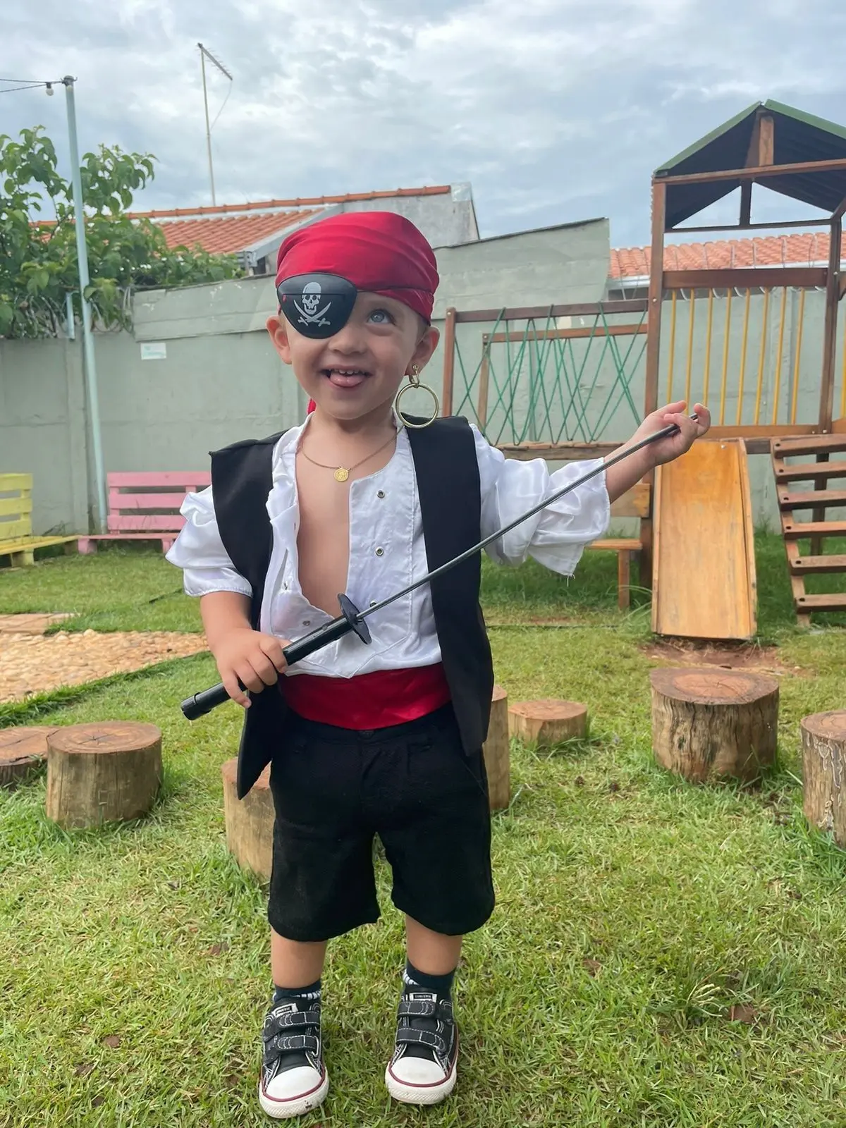 Criança fantasiada de pirata com tapa-olho, bandana vermelha, colete preto e espada de brinquedo.