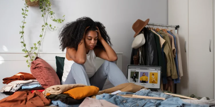 O que usar no ENEM? Veja dicas para o visual perfeito na hora da prova 1 Estudante sentada na cama cercada por roupas, planejando o que vestir no dia do ENEM.