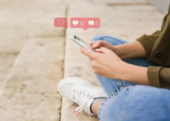 Mulher interagindo com o celular, acompanhada de curtidas e comentários nas redes sociais, simbolizando a conexão digital em outubro.