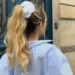 Penteado prático para dias quentes, com cabelo preso em um rabo de cavalo alto e preso por um scrunchie branco.