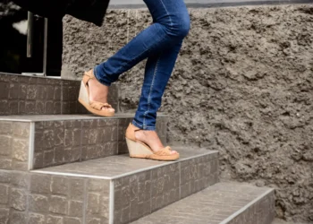 Salto anabela está em alta novamente! Veja como usar nos seus looks 11 Mulher usando sandálias anabela bege enquanto sobe escadas de pedra.
