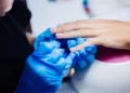 Unhas de gel: 10 dicas essenciais para manter suas unhas bonitas e saudáveis 10 Profissional aplicando esmalte de gel em unha de cliente com luvas azuis.