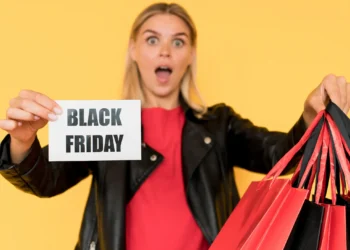 Mulher surpresa segurando sacolas de compras com cartaz escrito Black Friday — moda e beleza em destaque.