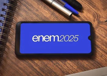 Tela de celular exibindo o logotipo do ENEM 2025 sobre uma mesa com cadernos e canetas.